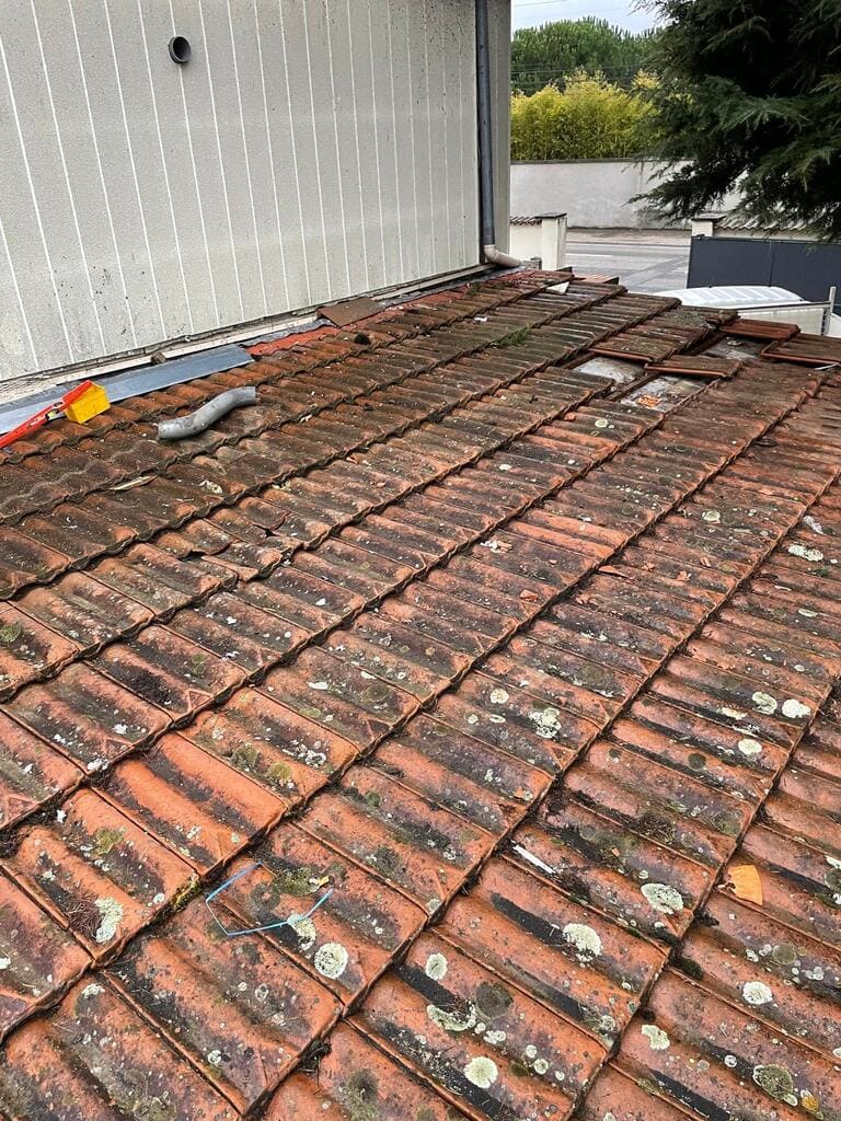 Toiture en tuiles de terre cuite usée, couverte de lichens, avec des tuiles déplacées et cassées sur une maison à Meyzieu couvreur Matray L Fils