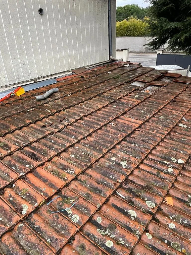 Toiture en tuiles de terre cuite usée, couverte de lichens, avec des tuiles déplacées et cassées sur une maison à Meyzieu couvreur Matray L Fils